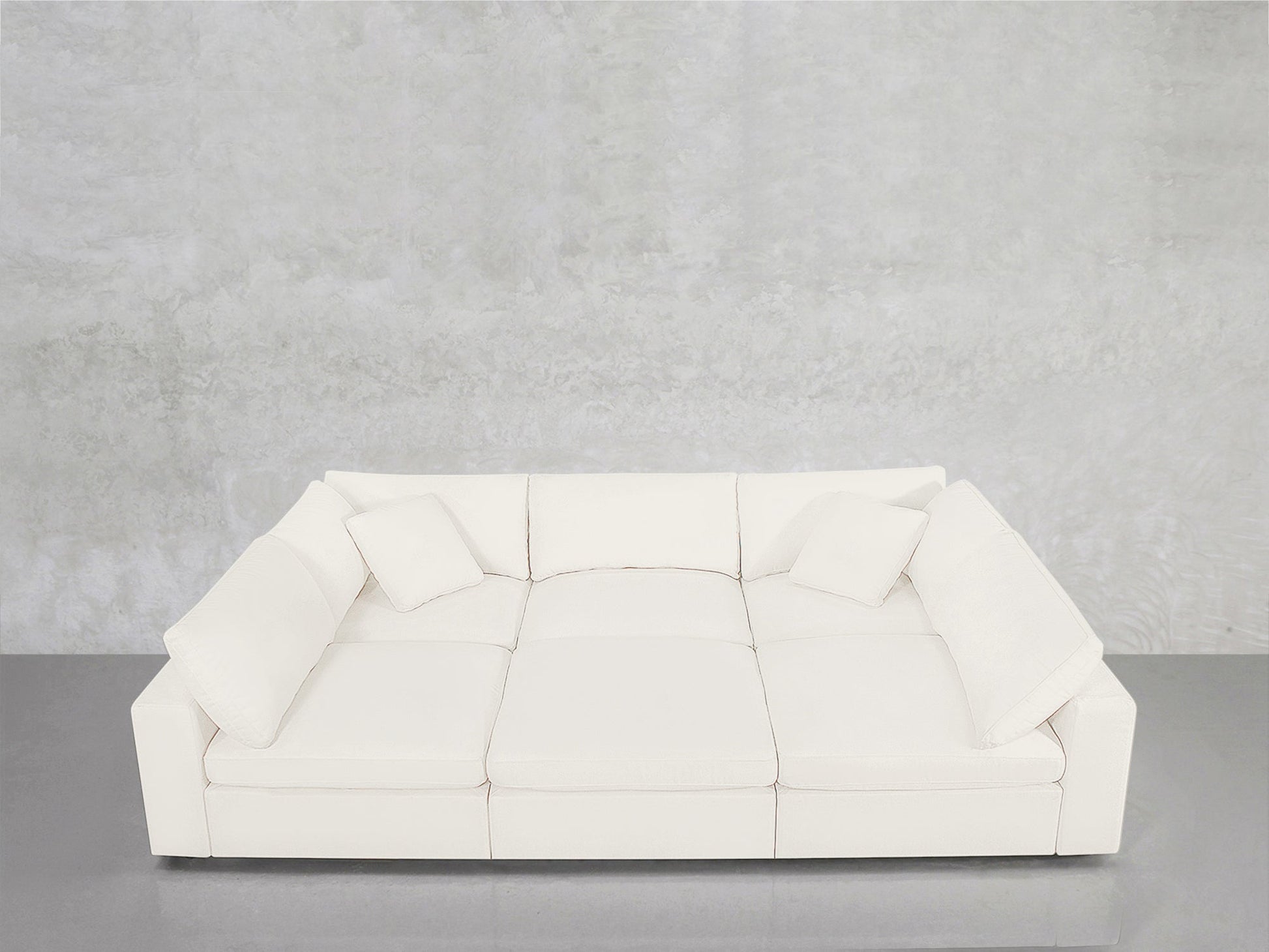 A modern white 6-Seat Modular Pit with three seat cushions and four matching pillows sits against a light gray textured wall and glossy gray floor.