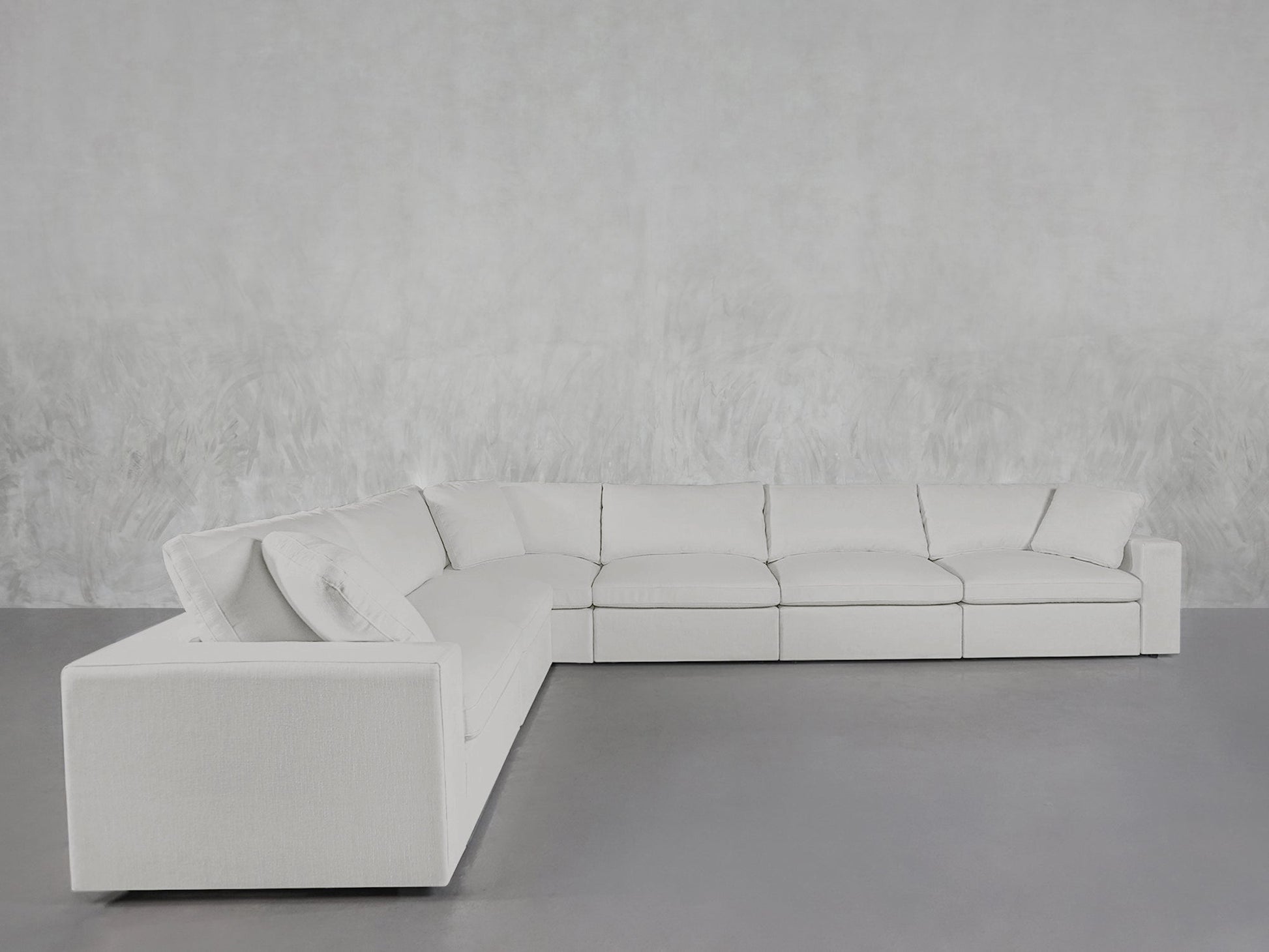 A 6-Seat Modular Corner Sectional with modern design and clean lines is set in a minimalistic room featuring a light gray floor and textured pale gray wall.