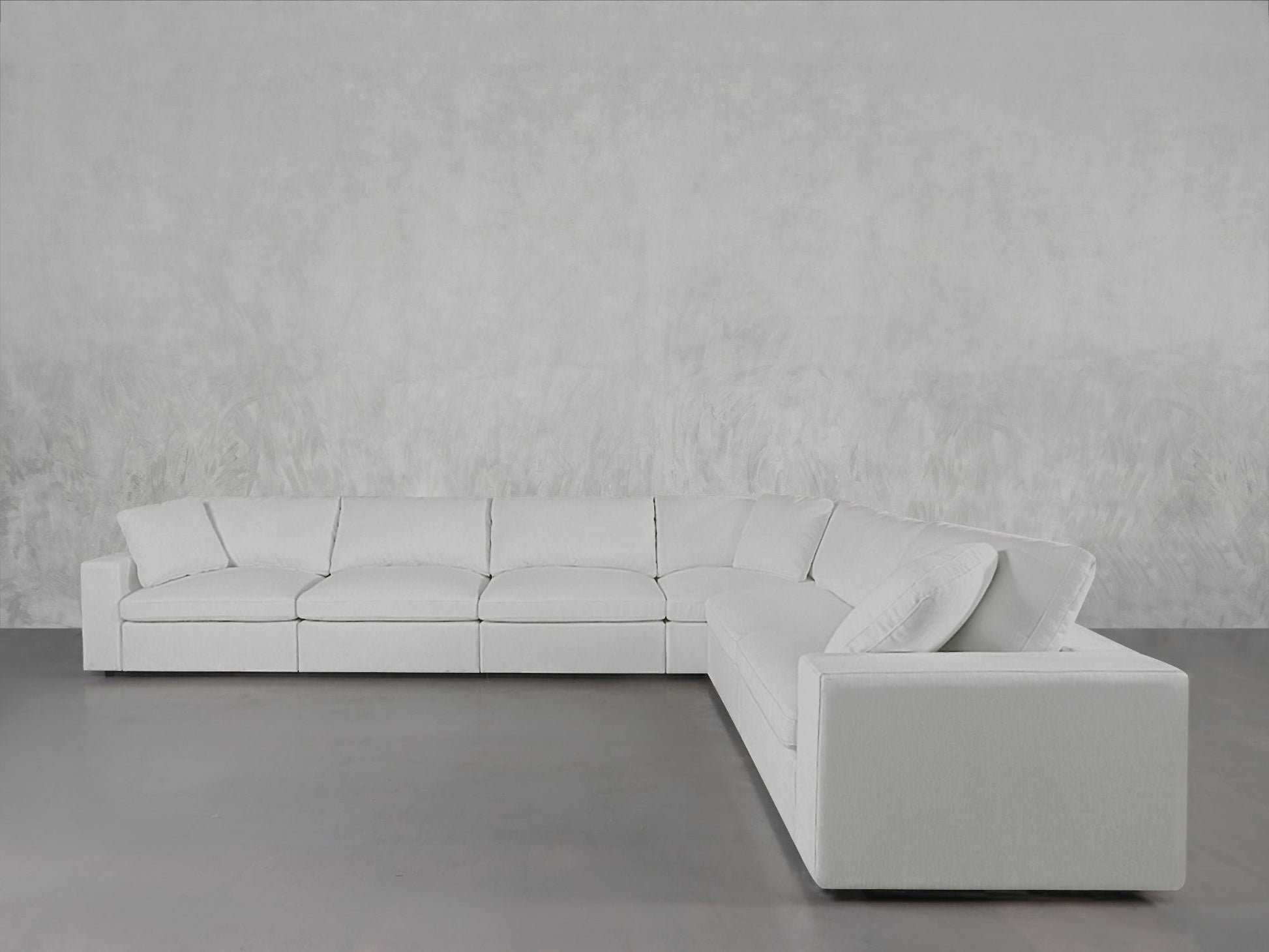 The 6-Seat Modular Corner Sectional, upholstered in light gray fabric, is arranged against a textured pale gray wall on a smooth gray floor.