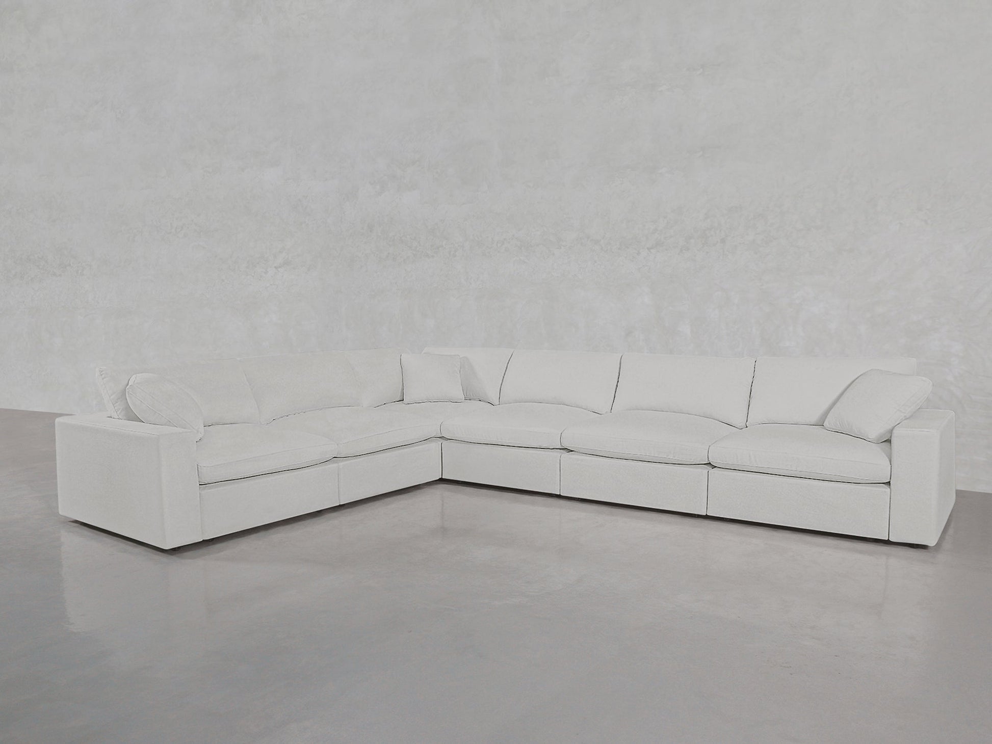 The 6-Seat Modular Corner Sectional, featuring plush cushions in white, sits on a smooth gray floor against a light textured wall in a minimalist, modern space.