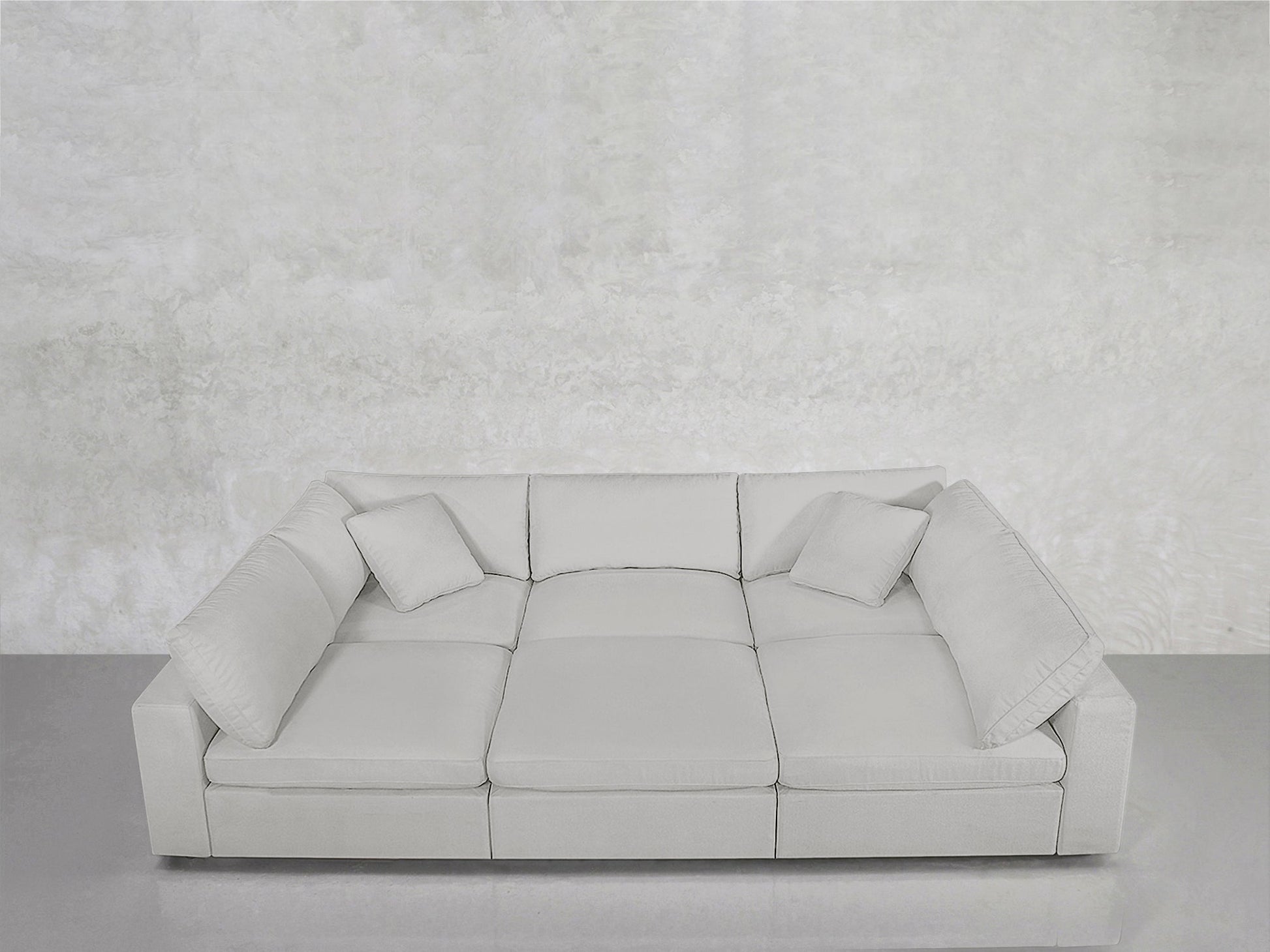 The 6-Seat Modular Pit, in modern light gray, features three seat cushions and three matching pillows, set against a textured light gray wall and gray floor for a minimalist, monochromatic aesthetic.