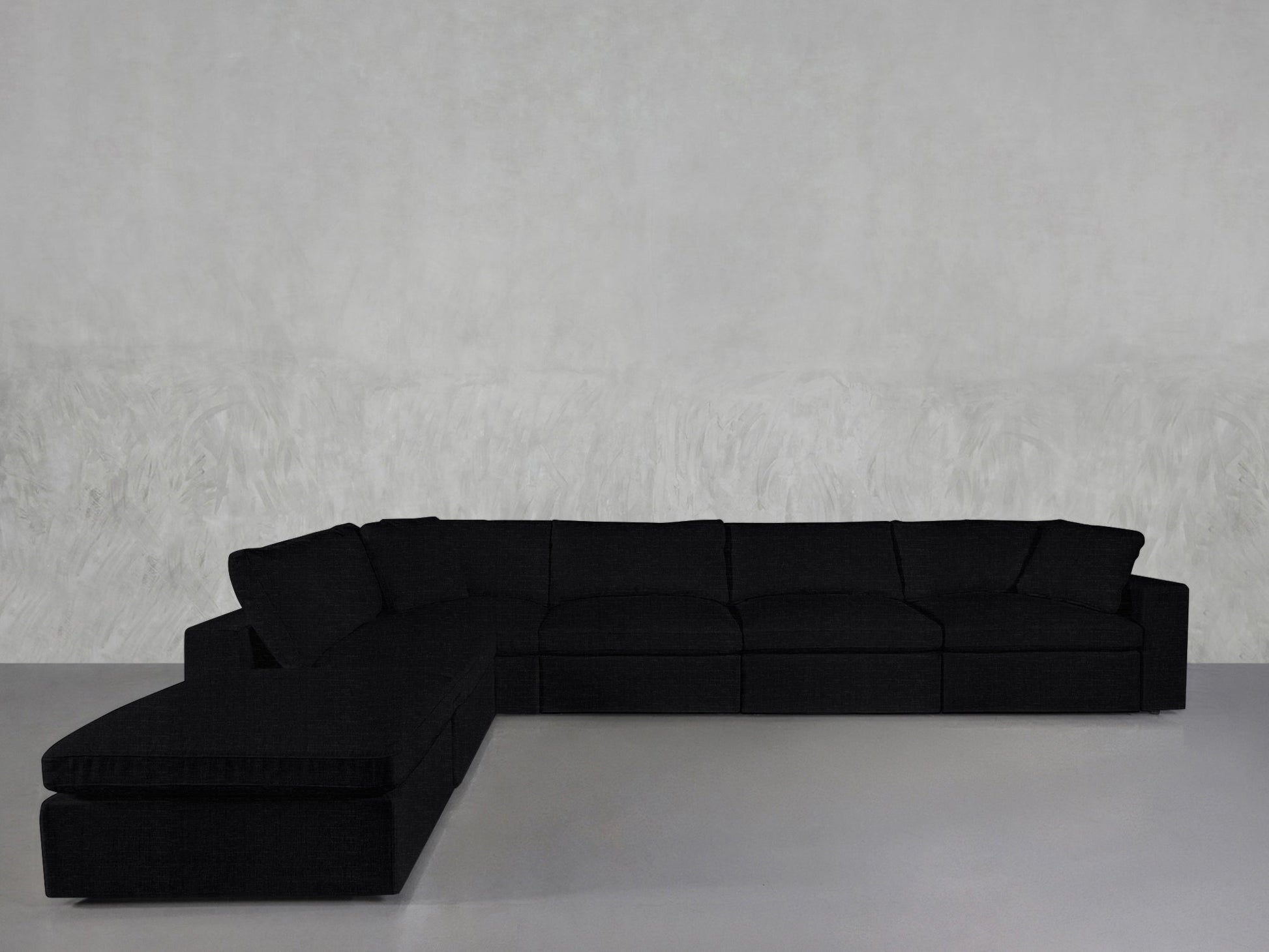 A spacious black 6-Seat Modular Corner Lounger Sectional with cushions sits in a minimalist room featuring a light gray textured wall and a smooth gray floor.