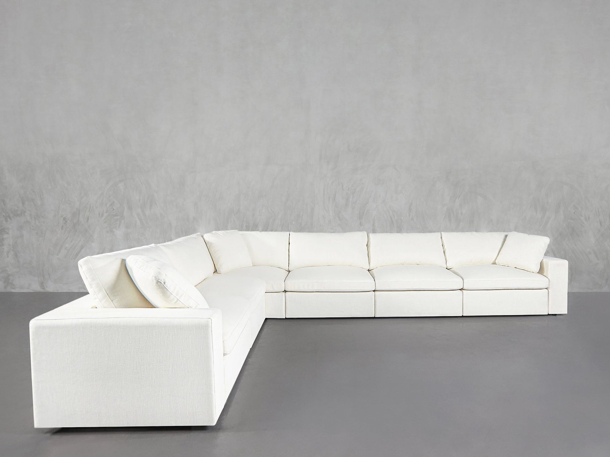 A 6-Seat Modular Corner Sectional in modern white with plush cushions sits against a plain light gray wall on a smooth gray floor.