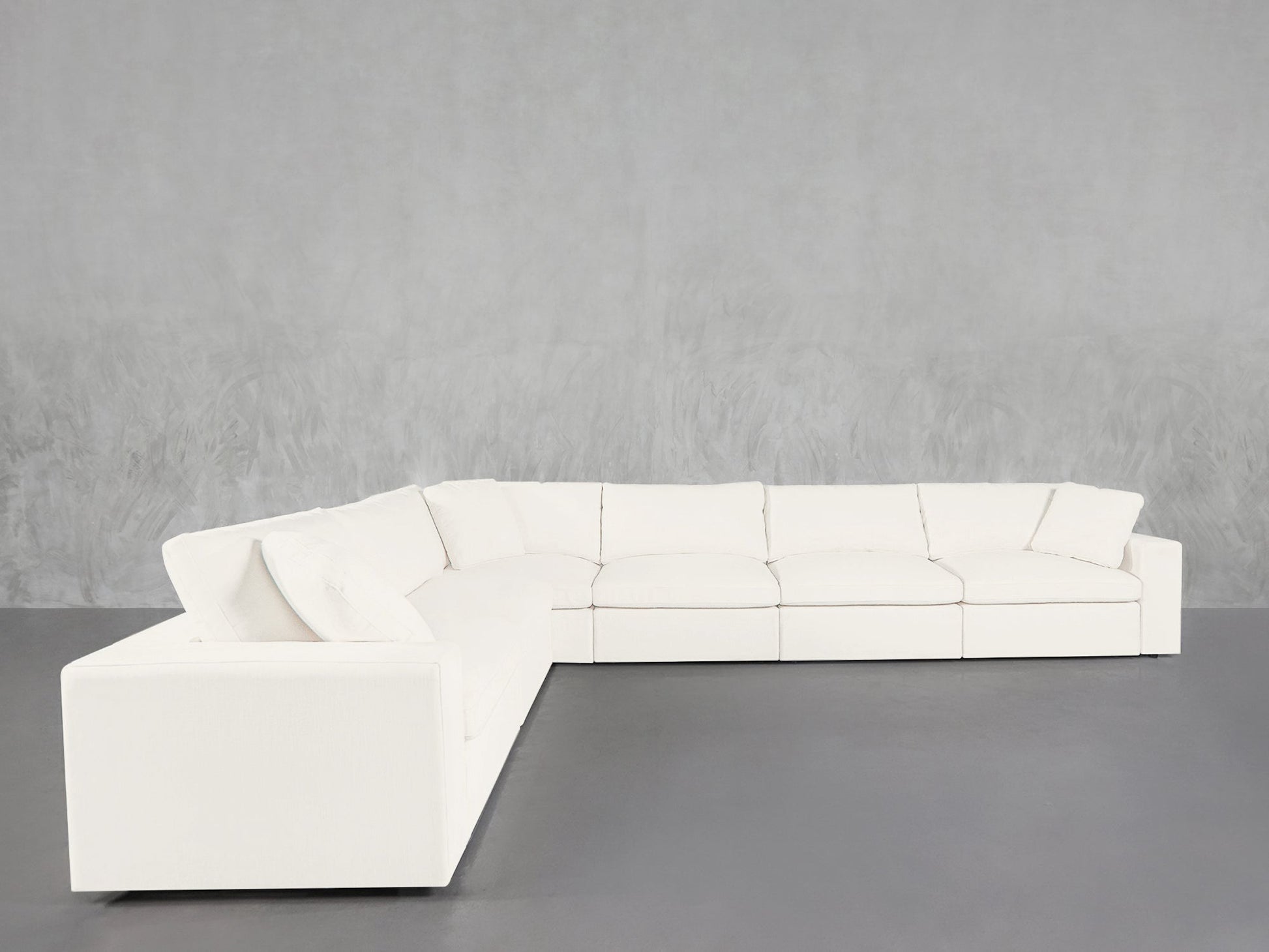 A 6-Seat Modular Corner Sectional with clean lines in white sits on a dark gray floor against a light gray textured wall.