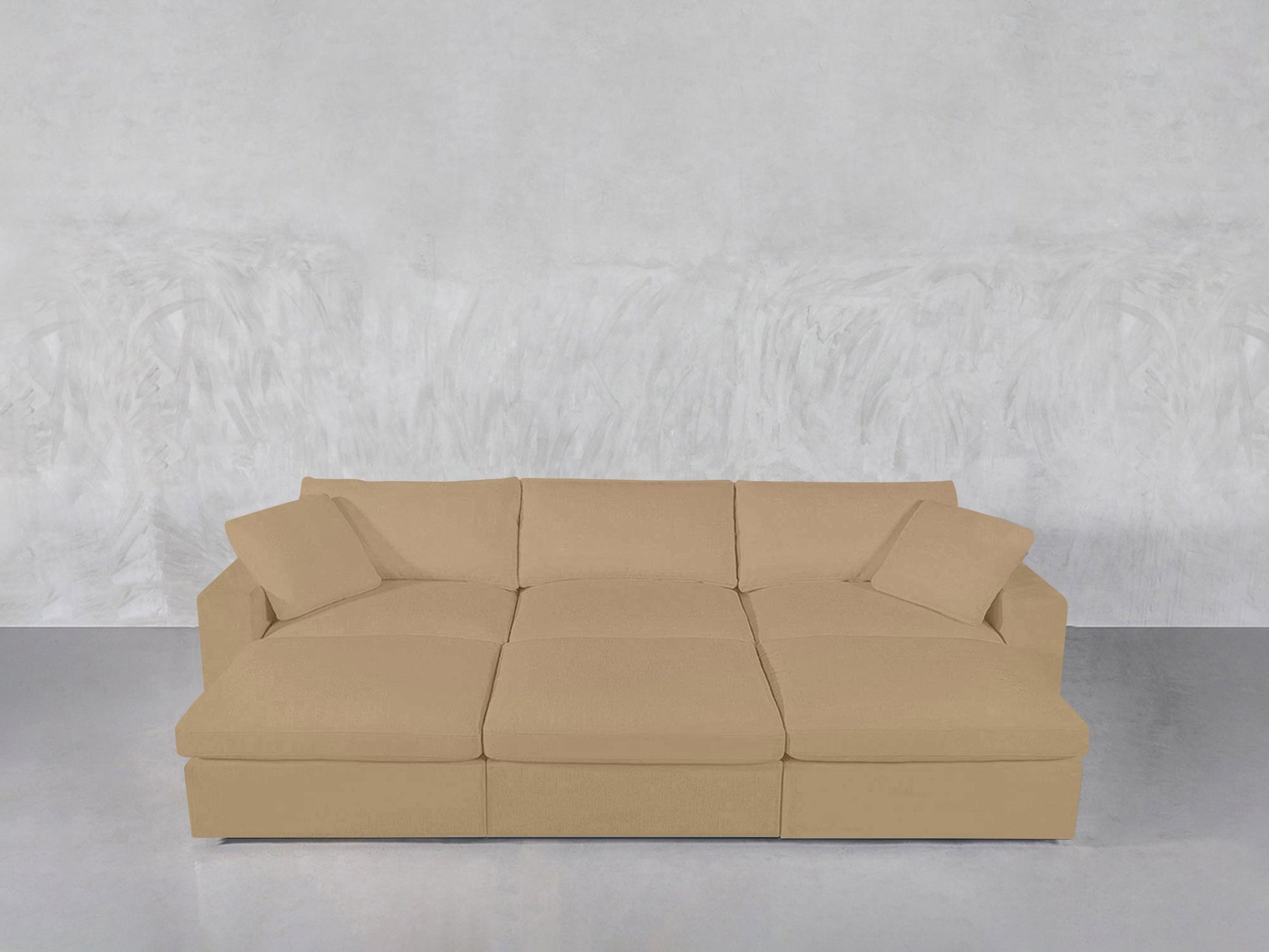 A beige 6-Seat Modular Daybed with matching cushions sits against a light gray textured wall on a smooth, reflective floor.