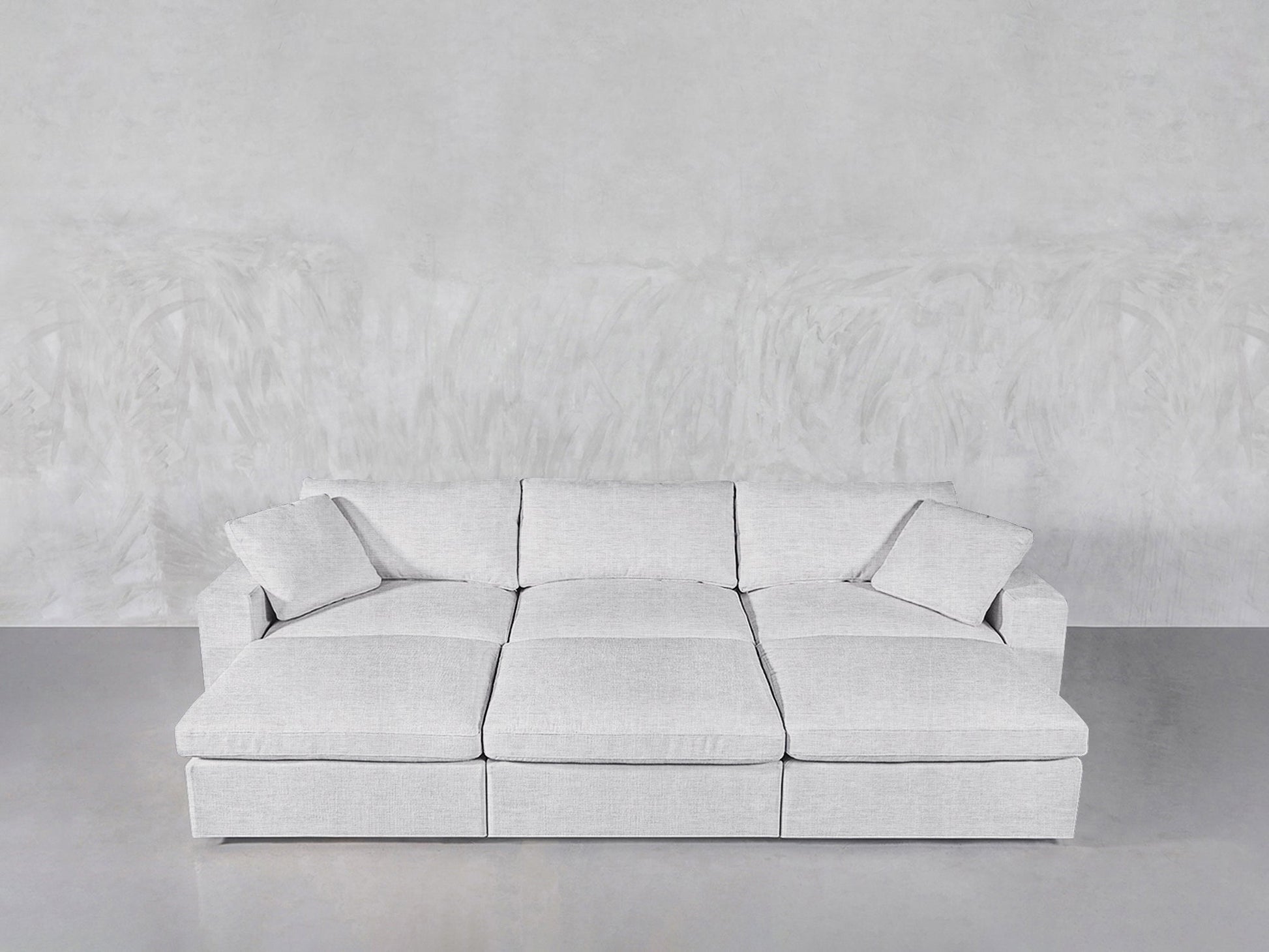 A modern, light gray 6-Seat Modular Daybed with matching cushions is set against a textured light gray wall atop a smooth concrete floor.