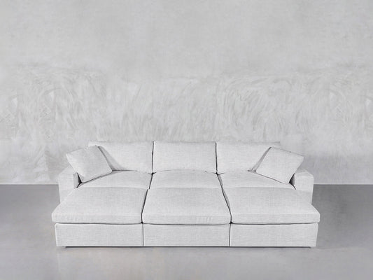 A modern, light gray 6-Seat Modular Daybed with matching cushions is set against a textured light gray wall atop a smooth concrete floor.