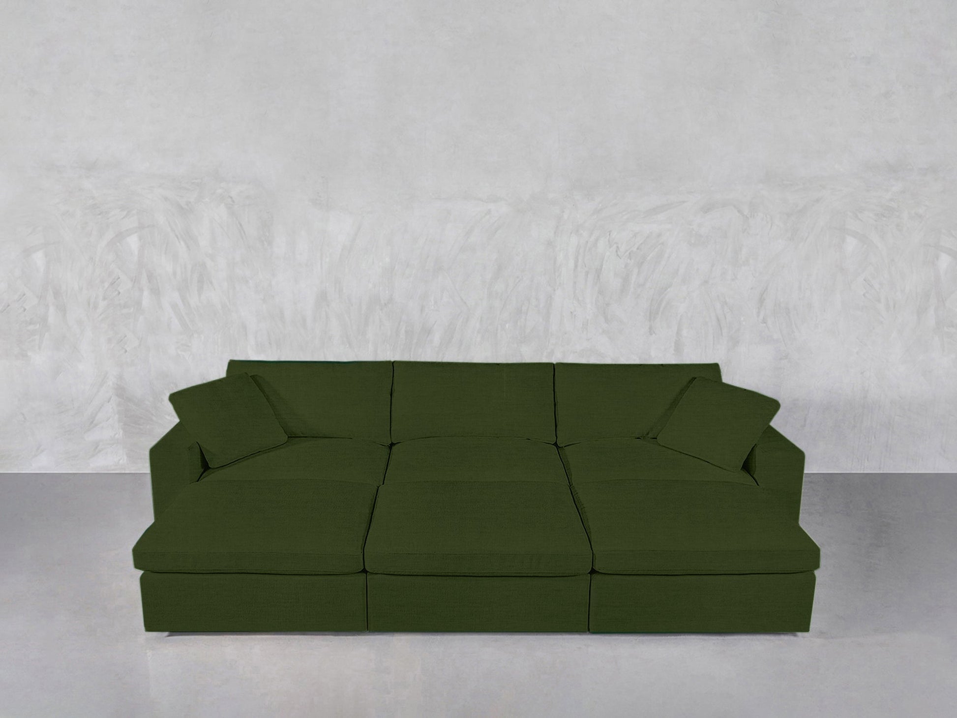 A green 6-Seat Modular Daybed with two matching cushions sits against a light gray textured wall on a smooth, reflective floor.