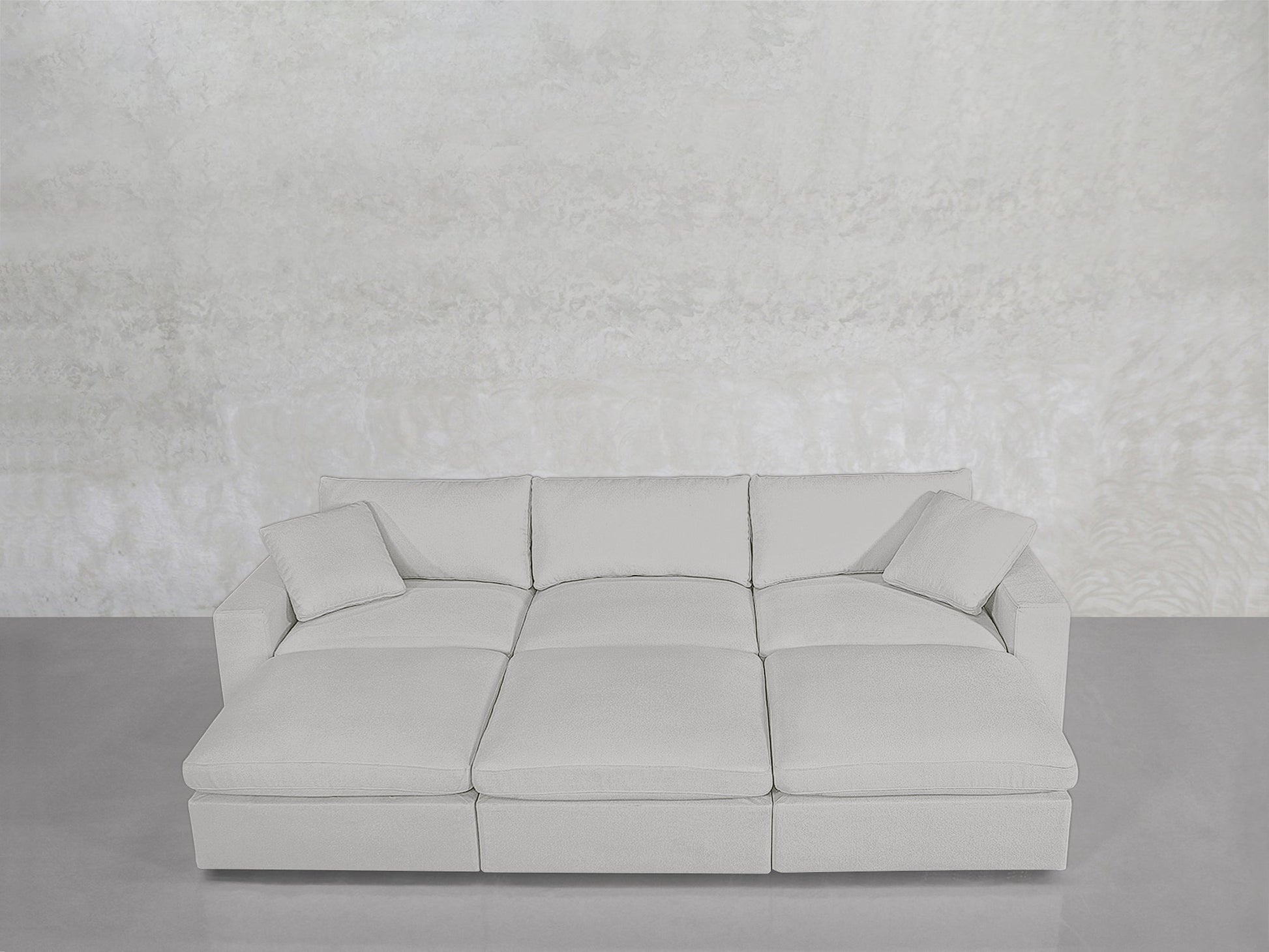 A modern, light gray 6-Seat Modular Daybed with matching cushions, set against a textured light gray wall and a smooth gray floor.