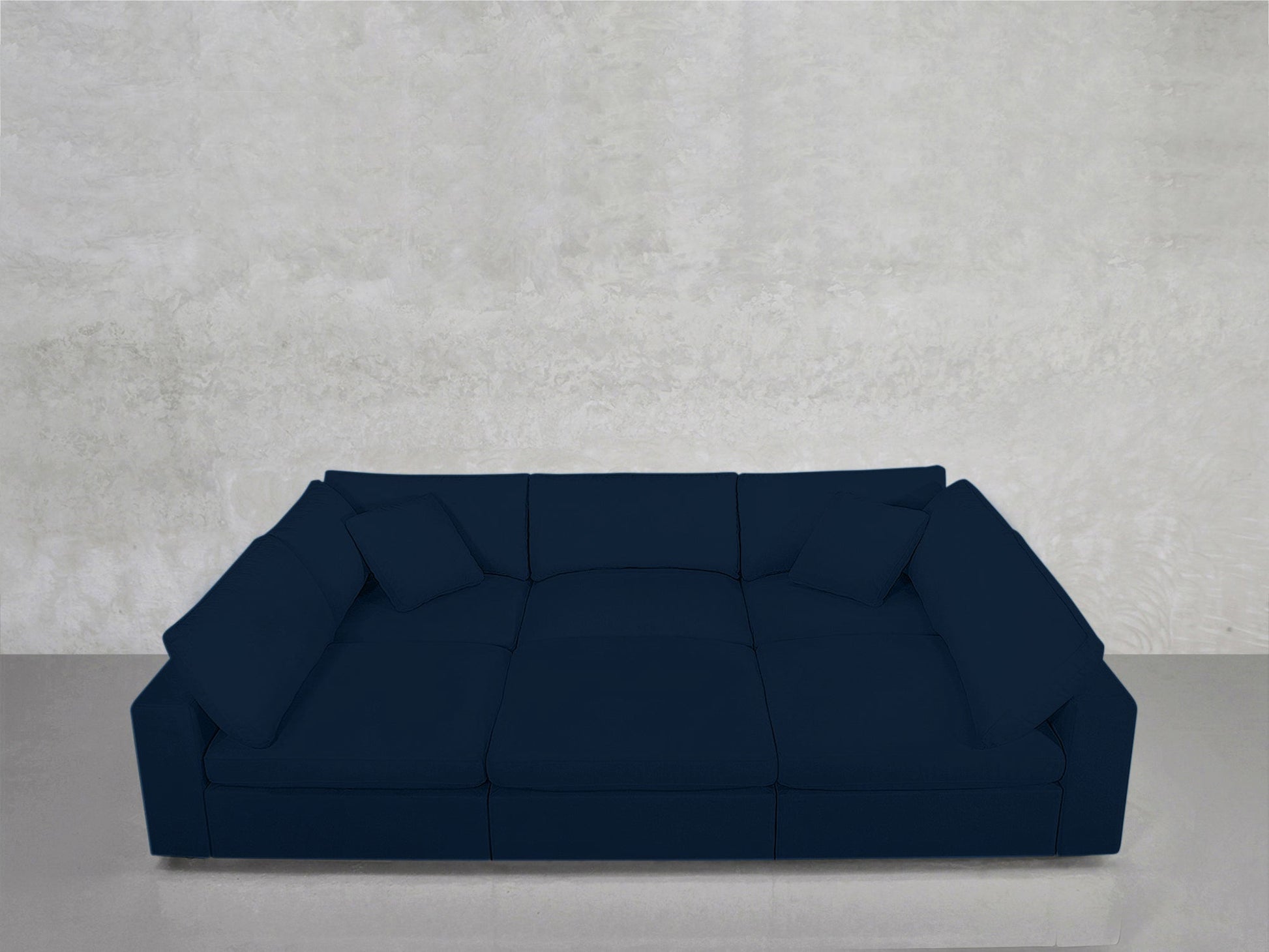 A 6-Seat Modular Pit in dark blue with square cushions sits against a light gray textured wall on a glossy floor.