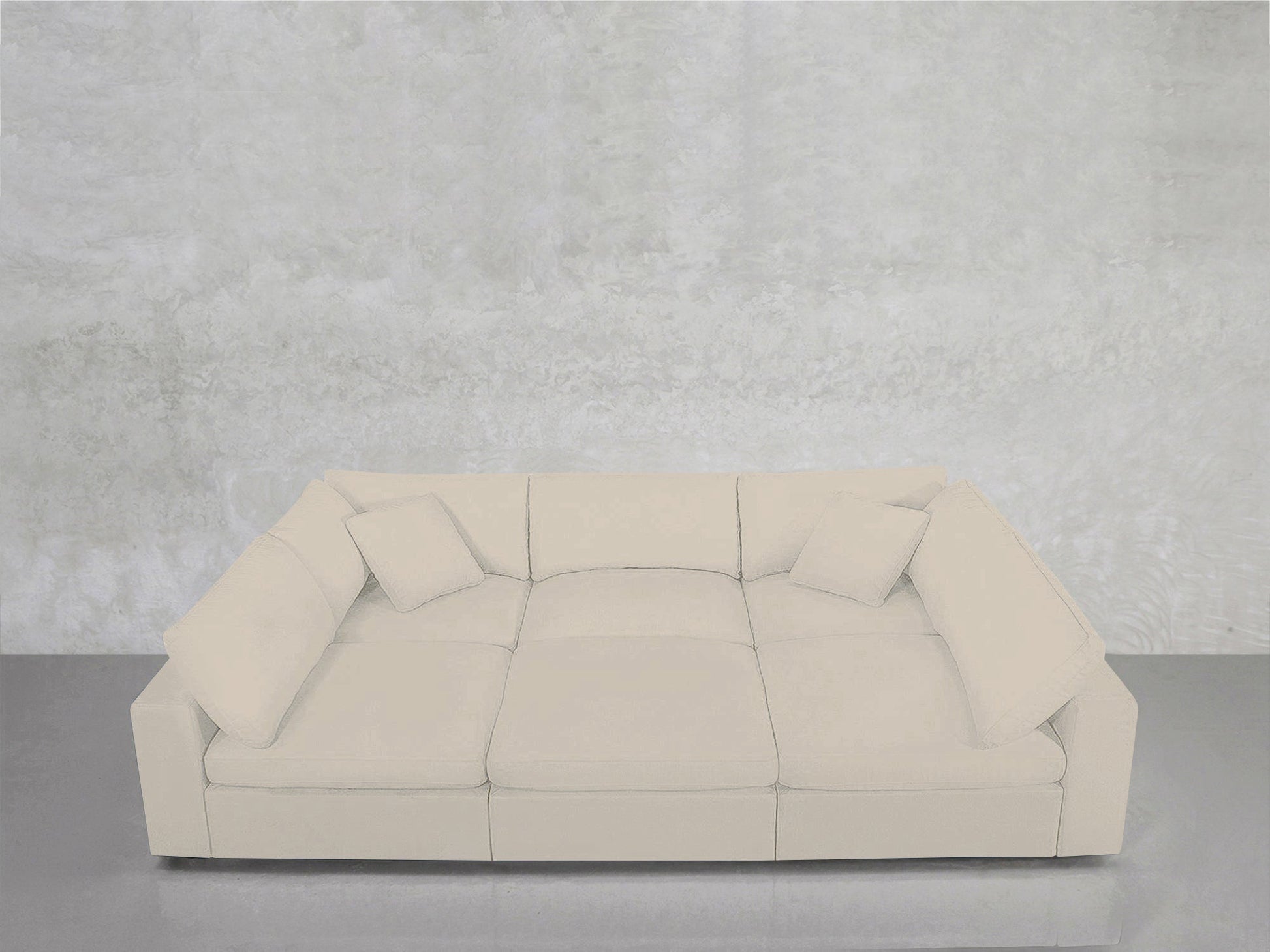 A contemporary 6-Seat Modular Pit in white, complete with four matching square cushions, is positioned against a light gray textured wall atop a glossy gray floor.