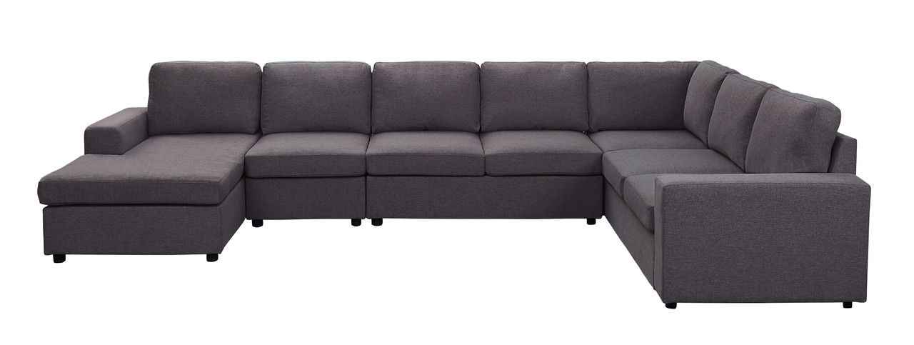 The Tifton - Linen 7 Seat Reversible Modular Sectional Sofa Chaise is a large L-shaped sofa in dark gray fabric, with cushioned seats and backs, a reversible chaise lounge, and armrests on each end.