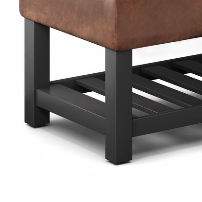Close-up of the Cosmopolitan Storage Ottoman Bench With Open Bottom, showcasing its black metal leg, brown upholstered cushion, and open slatted shelf. The modern design features clean lines against a white background.
