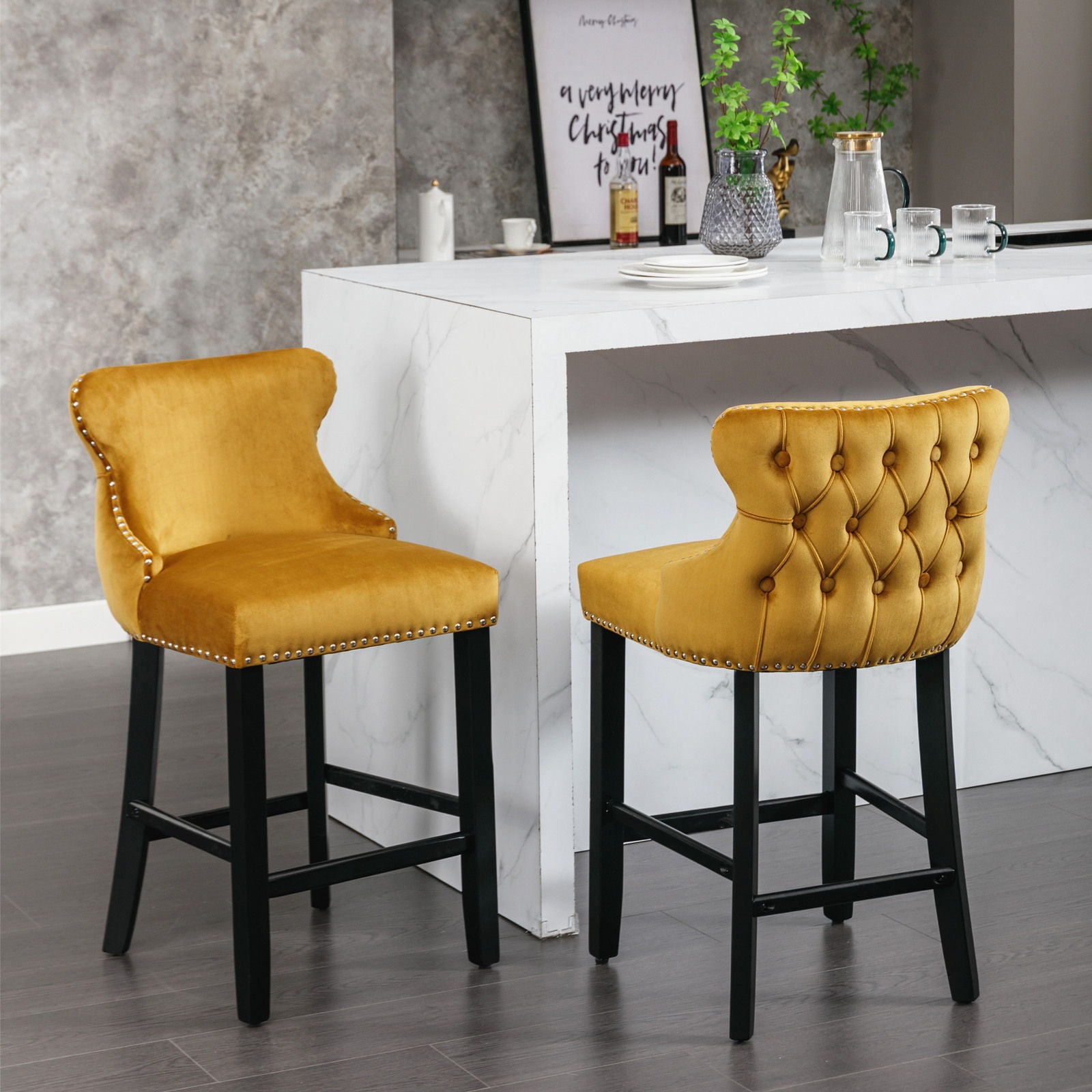 A pair of Contemporary Velvet Upholstered Wing-Back Barstools with tufted backs, wooden legs, and chrome nailhead trim are set by a white marble kitchen island in a modern kitchen with gray walls and sleek decor.