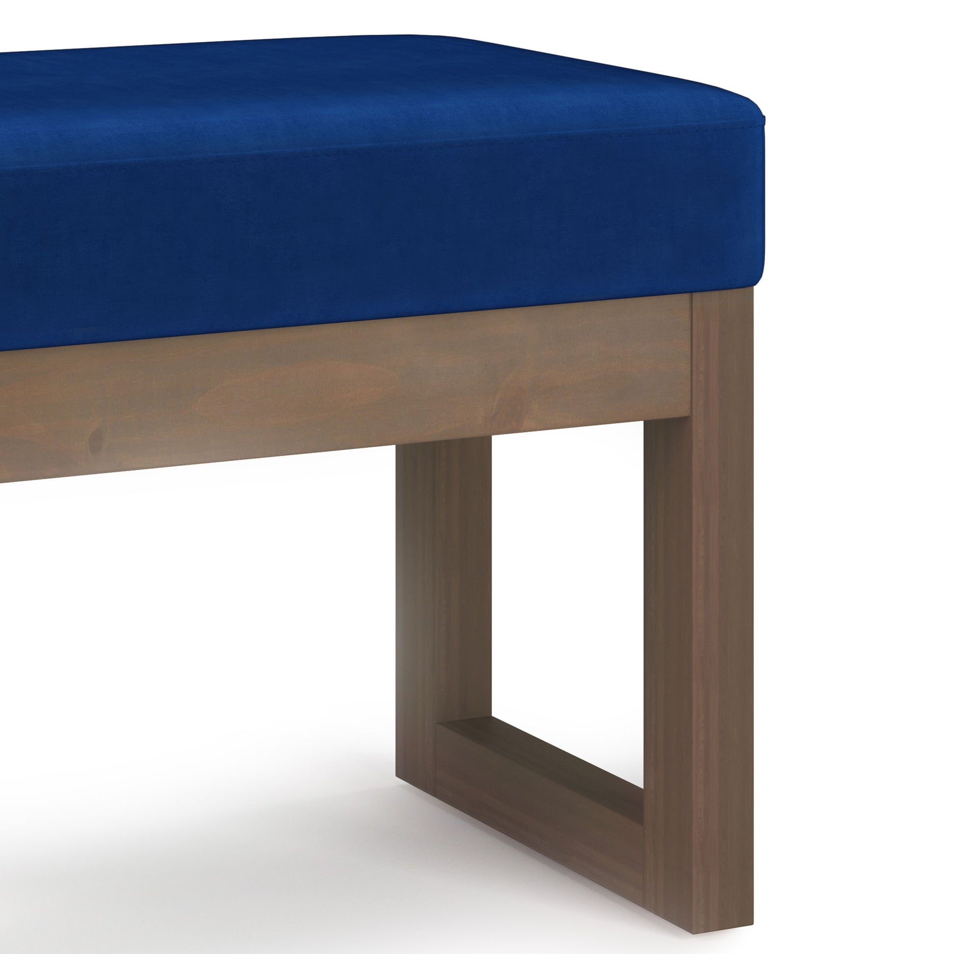 A close-up of the Milltown - Upholstered Ottoman Bench, showcasing its deep blue cushioned seat and wooden rectangular legs in a simple, modern design against a white background.