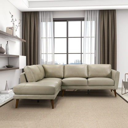 A modern living room with the Benson Sectional Sofa With Chaise in light gray on a beige carpet, large window with sheer and dark curtains, and minimalist decor on white shelves.