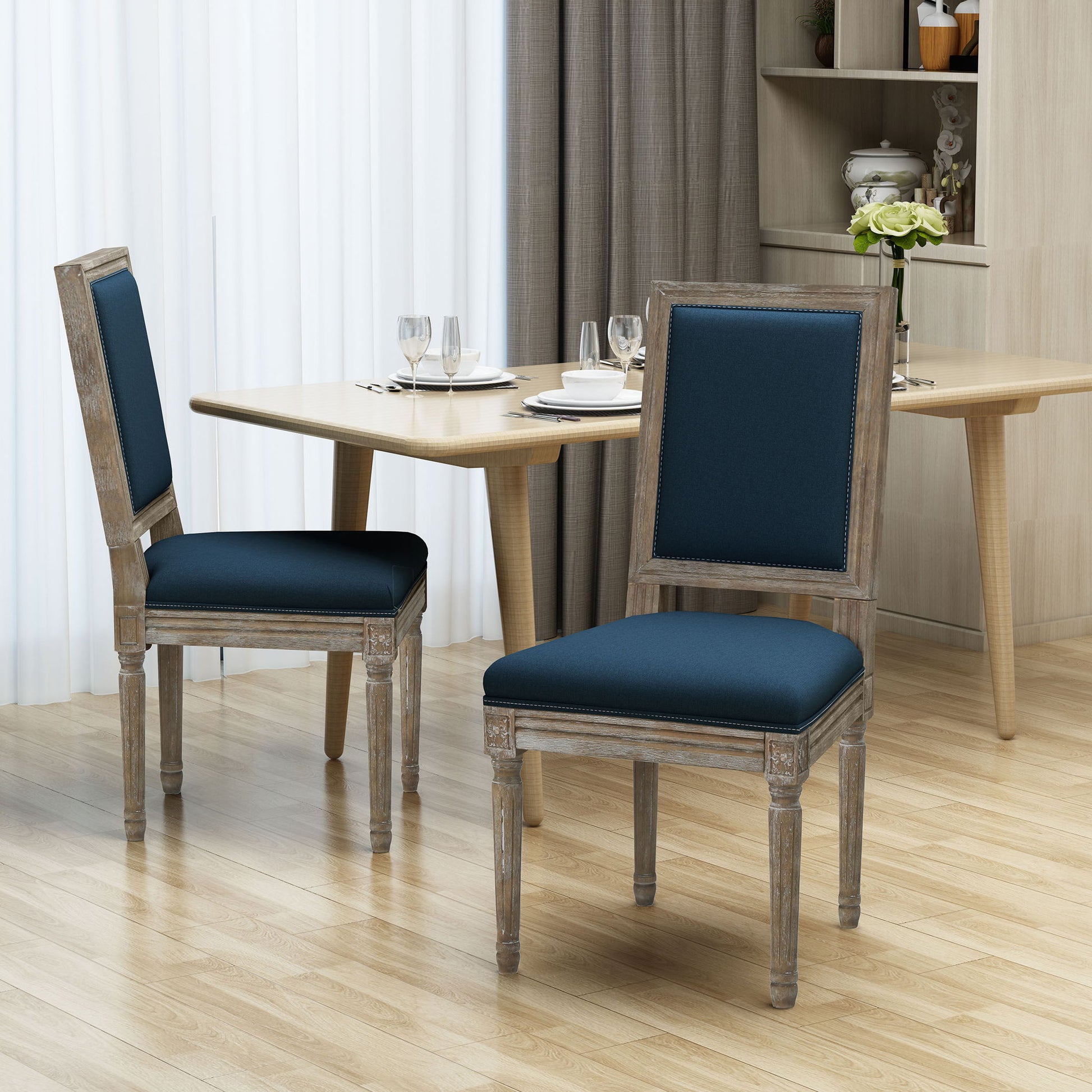 Two Traditional Style Dining Chairs With Fabric Upholstery, in dark blue, are placed near a light wood dining table set for a meal in a modern dining room featuring curtains and light wood flooring.