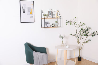 A modern, minimalistic room features a green armchair with a gray blanket, a white round table, and the Gardenia Wall Mounted Wall Storage for displaying decor, plus a framed abstract print and a potted plant in the corner.