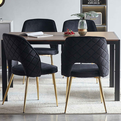 A modern dining area features a wooden table and four Velvet Dining Chairs With Metal Legs And Hollow Back, plus a small plant in a vase, an open book, and a plate of cherries on the table.