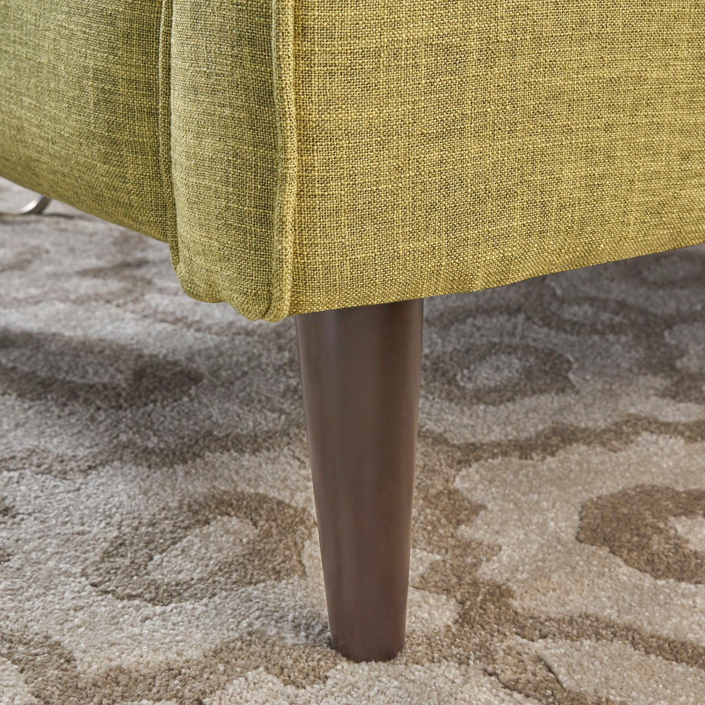 Close-up of the Mid-Century Modern Recliner With Button Tufted Waffle Stitch, showcasing its green upholstery and dark wood tapered leg on a beige and gray patterned carpet. The fabric texture and elegant leg design are clearly visible.