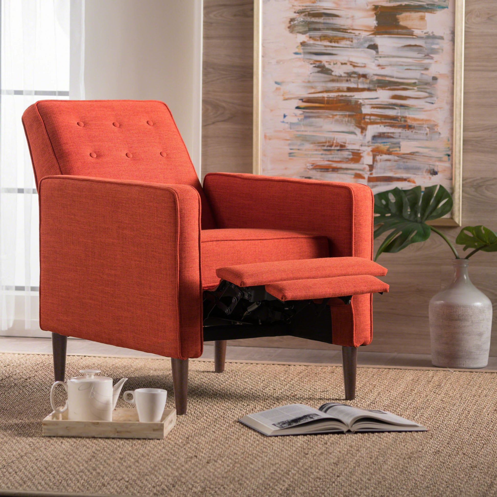 The Mid-Century Modern Recliner With Button Tufted Waffle Stitch in orange, featuring an extended footrest, sits on a woven rug near teacups and an open book, with abstract art and a vase of green leaves in the background.
