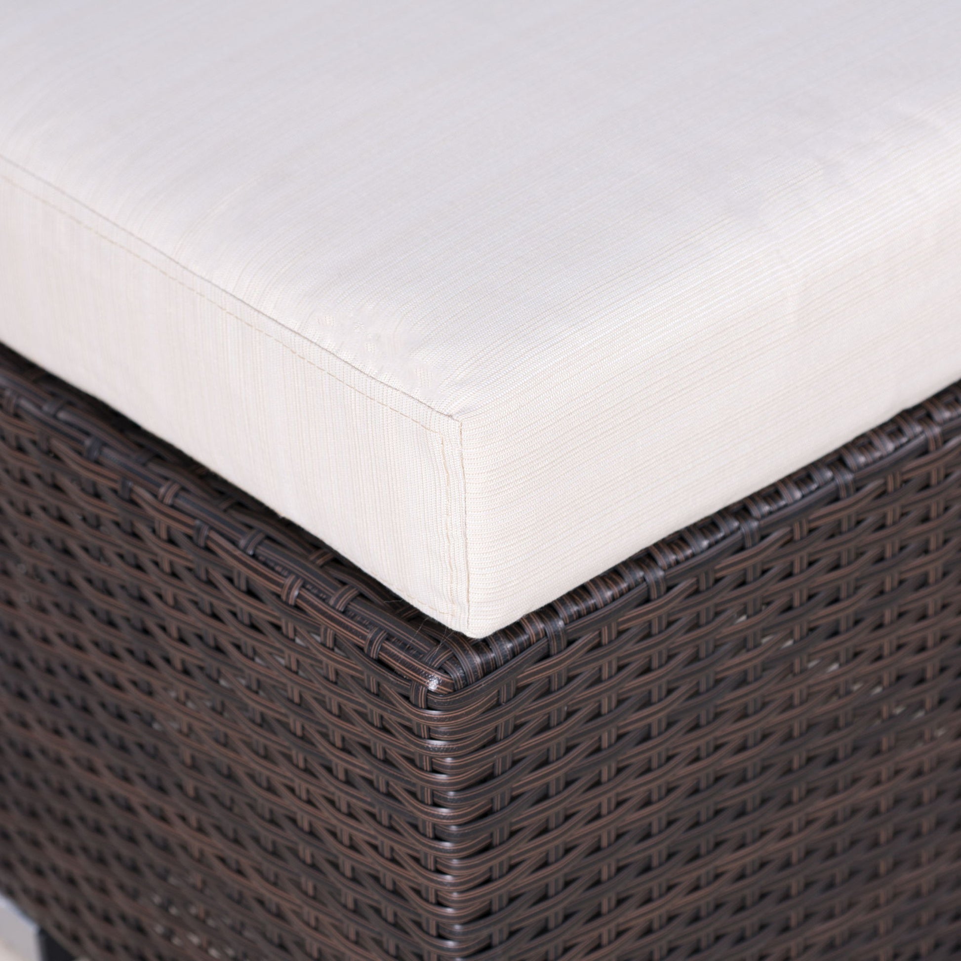 Close-up of the Santa Rosa - Outdoor Lounge Ottoman featuring a dark brown wicker base and a thick, light beige cushion. The woven texture and fabric details are clearly visible.
