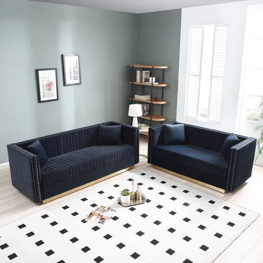 A modern living room featuring a Contemporary Vertical Channel Tufted Velvet Sofa Loveseat 2-piece set with 4 pillows, a white rug with black squares, round coffee table with magazines, standing lamp, corner bookshelf, and light green walls with art.
