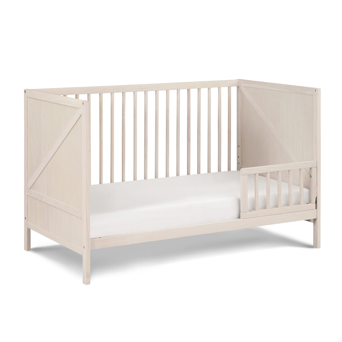 The Pixie Zen 3-in-1 Crib in Walnut features slatted sides, a minimalist light wood design, and includes one half-length right-side guardrail with a white mattress.