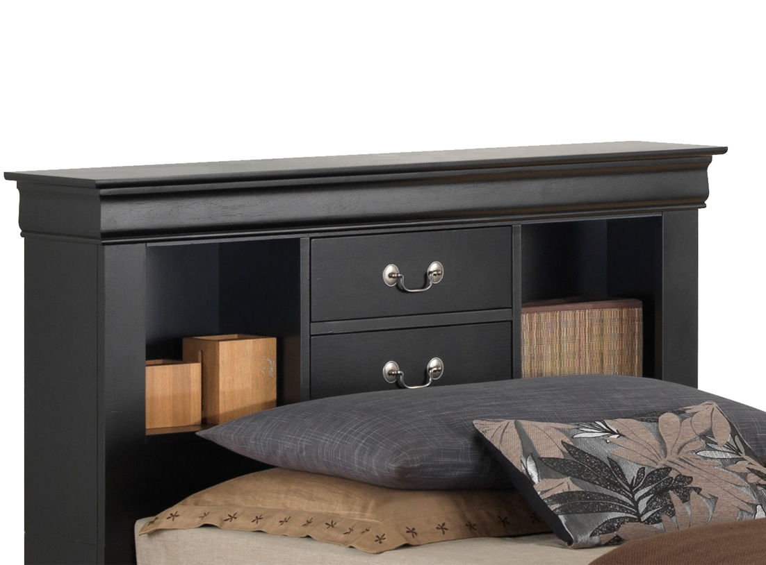 A close-up of the Louis Phillipe - Bookcase Storage Bed’s black wooden headboard shows two drawers and open shelves with books and decor. Pillows with leaf patterns on the bed are visible in the foreground.