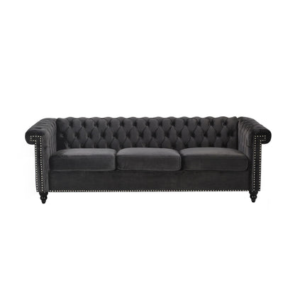 The Chesterfield Style 3 Seater Sofa features deep button tufting, black velvet upholstery, three seat cushions, nailhead trim on the arms and base, rolled arms, and dark wooden legs.