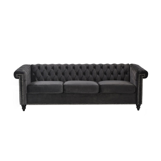 The Chesterfield Style 3 Seater Sofa features deep button tufting, black velvet upholstery, three seat cushions, nailhead trim on the arms and base, rolled arms, and dark wooden legs.