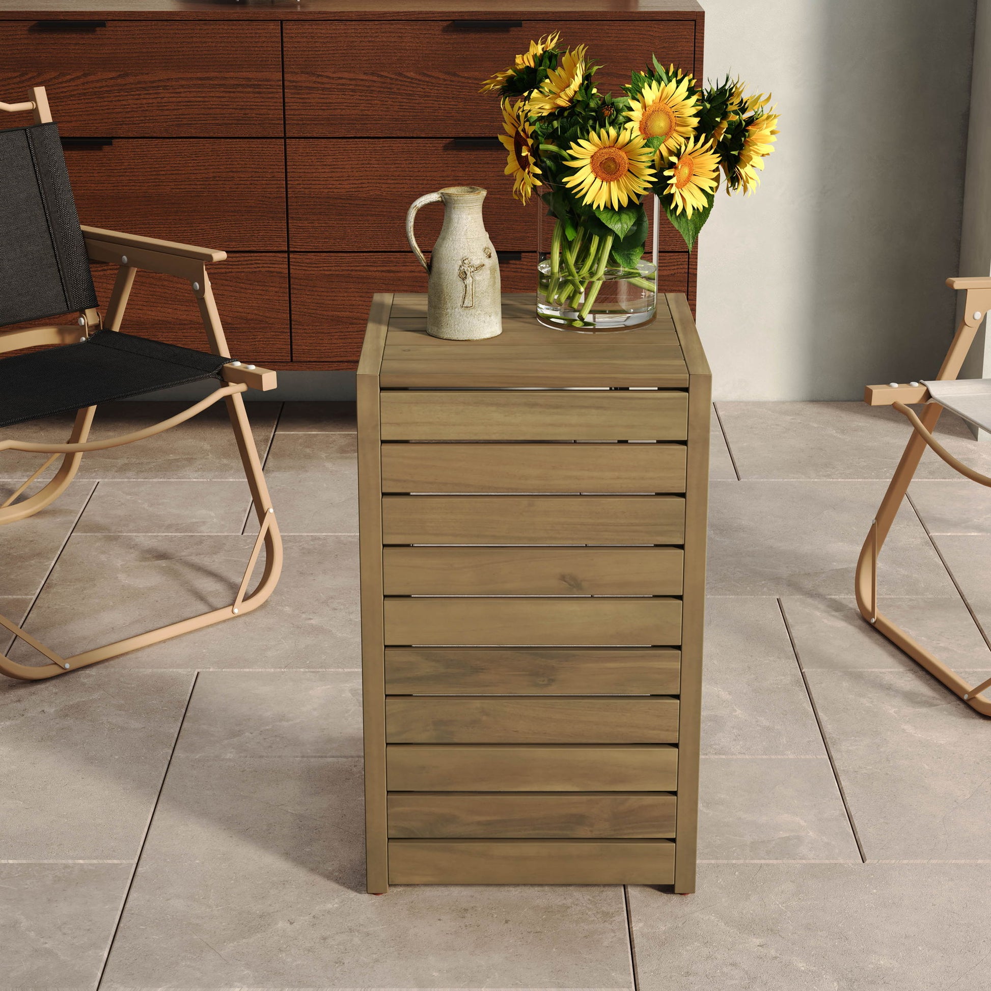 An Aluminum Outdoor C-Shaped Side Table for Patio holds a clear vase of sunflowers and a ceramic jug, flanked by two folding chairs on a tiled floor, with a wooden dresser visible in the background.
