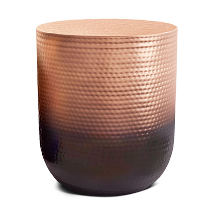 The Nova Handcrafted Metal Side Table features a round, drum shape and a textured metallic surface with a copper tone at the top that fades to an almost black base.