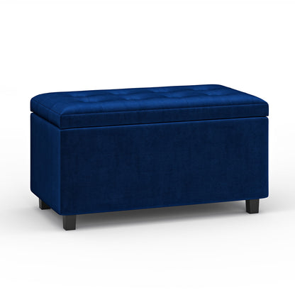 The Cosmopolitan Upholstered Storage Ottoman is a rectangular, dark blue bench with a tufted cushioned top, short black legs, and a modern design, displayed against a plain white background.
