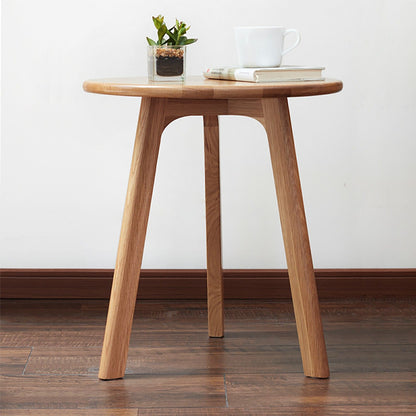 The Round Small End Table, Side Table For Bedroom & Balcony stands on three legs atop a wooden floor, holding a potted plant, two closed books, and a white cup with saucer. A plain white wall forms the background.