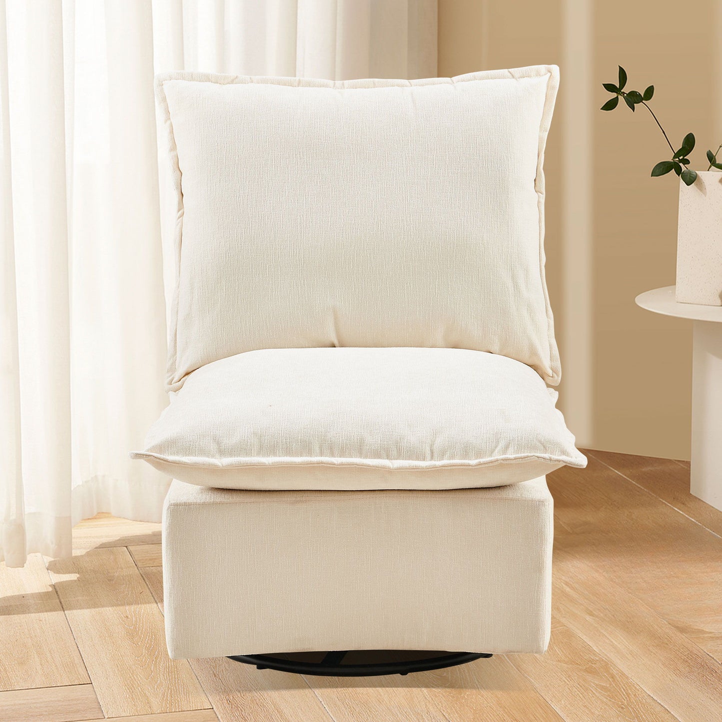 The Detachable Chenille Single 360 Swivel Rocking Rocker, a modern armless cream chair with plush cushions, sits on a light wood floor near sheer white curtains and a small table with a potted plant to the right.