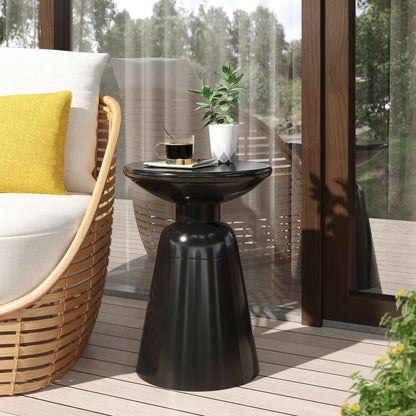 The Outdoor Modern Metal End Large Table in black holds a coffee cup, saucer, and a plant in a white pot. Beside it, a rattan chair with a yellow pillow is placed near a glass door with sheer curtains overlooking the outdoors.