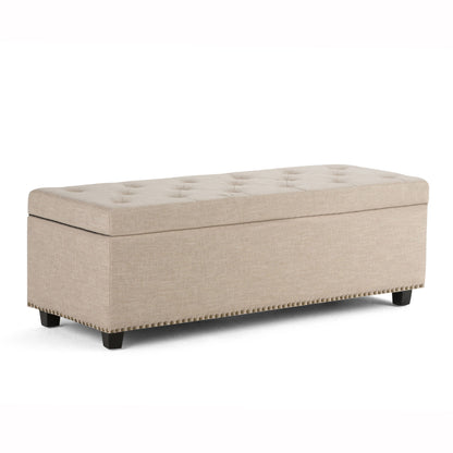 The Hamilton Upholstered Storage Ottoman features a beige fabric, button-tufted top, nailhead trim at the base, and short black wooden legs, shown against a white background.