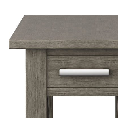 Close-up of the corner of the Kitchener - Handcrafted Table in gray wood, featuring a visible wood grain and a drawer with a silver handle.