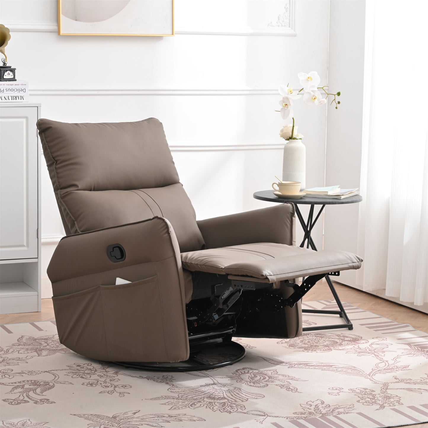 The 360° Modern Small Rocking Swivel Recliner Chair with Side Pocket sits beside a round side table holding a vase of white flowers and a teacup in a bright, elegant living room with white walls and sheer curtains.