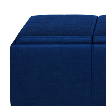 A close-up of the Avalon - Upholstered Storage Ottoman in blue, featuring a soft velvet finish and two cushioned tops, set against a white background.