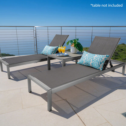 Two gray Outdoor Patio Chaise Lounges with 5 reclining positions and blue patterned pillows are on a patio with an ocean view. A small table with drinks and a plant sits between them. Text in the corner reads, “*table not included.”.