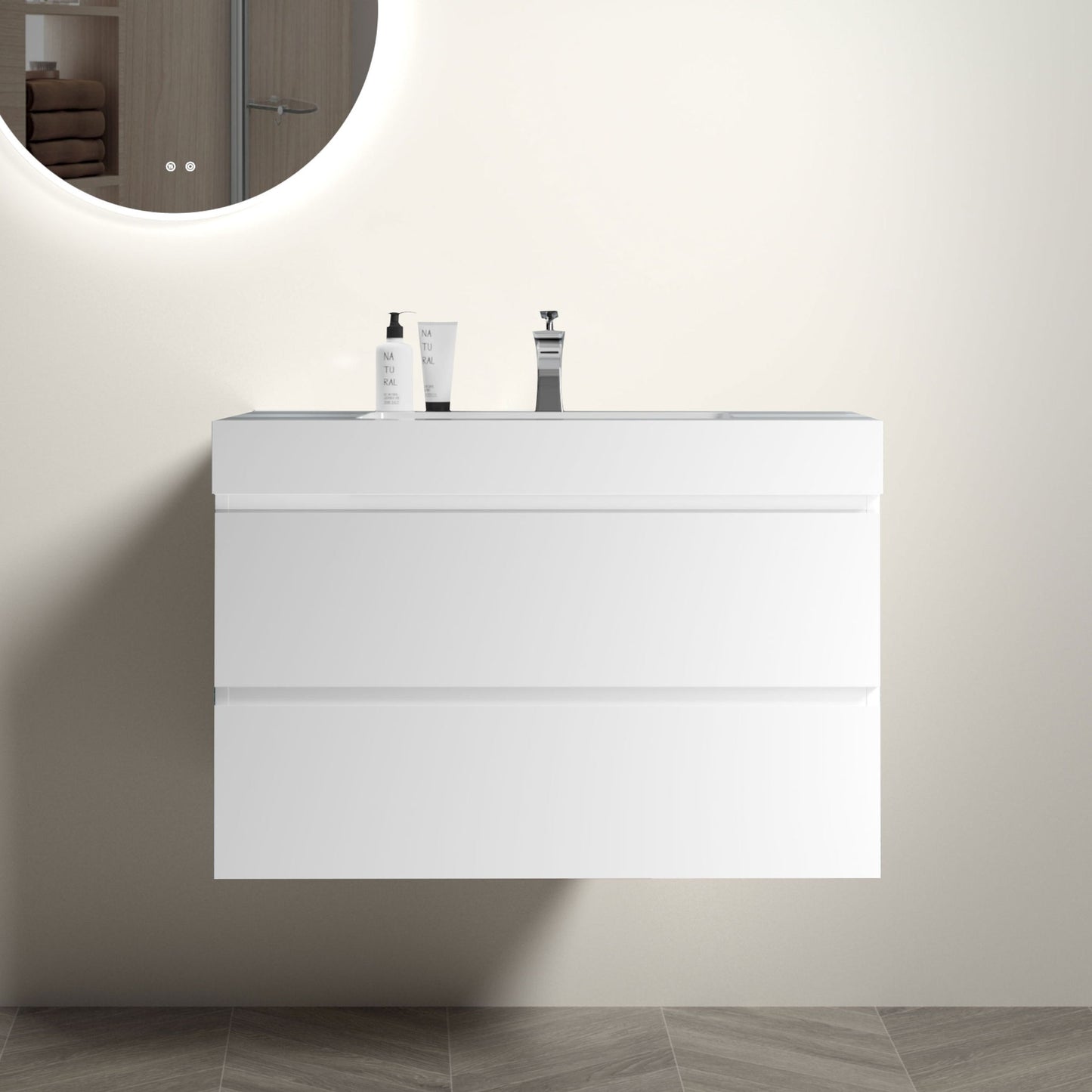 The Alice Bathroom Vanity, a modern wall-mounted floating design with large storage and a sleek one-piece sink basin (no drain or faucet), is paired with a round mirror reflecting folded towels and a wooden cabinet door.