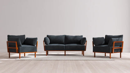 The Indoor Jack 2-Seater Sofa + Armchair Set in Balsa features a sleek and modern design with a dark gray finish. It includes a sofa and two matching armchairs with elegant wooden frames, all arranged on a light-colored rug atop a wooden floor, set against a plain, light gray wall.