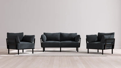 A contemporary living room ensemble showcasing the Indoor Jack 2-Seater Sofa + Armchair Set in Balsa, with both pieces set on a light-colored hardwood floor. The sleek black frames perfectly complement the dark gray upholstery, all arranged on a neutral area rug against a plain beige wall.