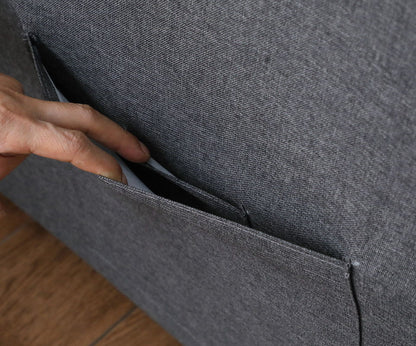 A hand places a smartphone into the side pocket of the Zoey Convertible Sleeper Chair, which sits on a wooden floor.