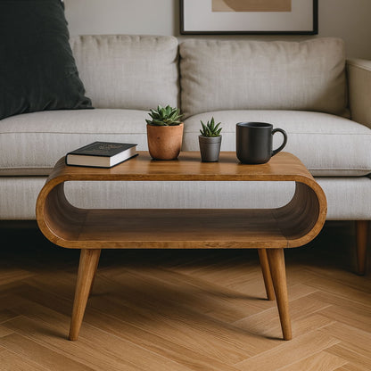 The Solid Wood Open Coffee Table with rounded edges holds two potted succulents, a closed book, and a black mug. Behind it is a light-colored sofa set on a wooden floor.