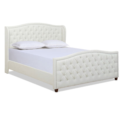 The Marcella - Upholstered Shelter Headboard Bed Set features a white tufted headboard and footboard with nailhead trim, two white pillows on a white mattress, and stands on short, dark wooden legs.
