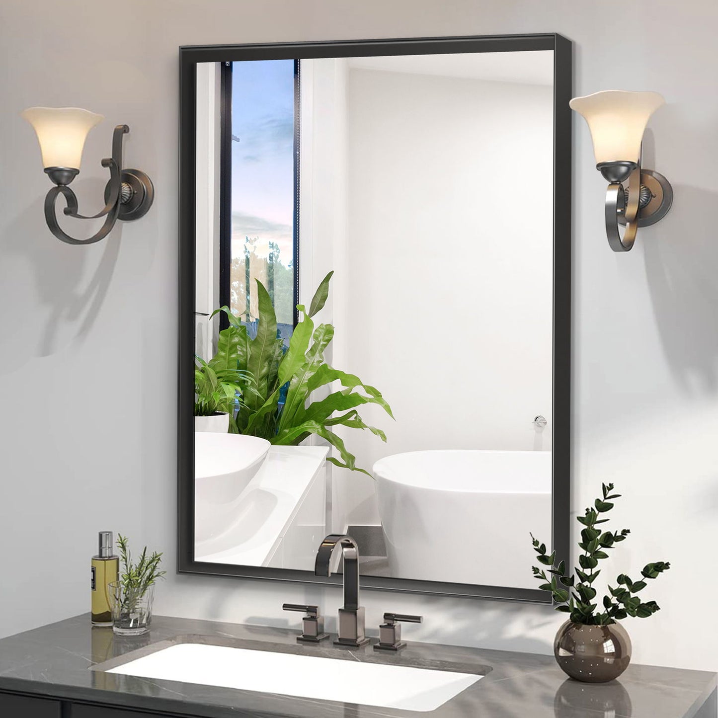 A Rectangular Bathroom Mirror with a square angle metal frame is mounted above the sink, flanked by two sconces. The mirror reflects a bathtub, window, and green potted plant, while toiletries rest on the counter.