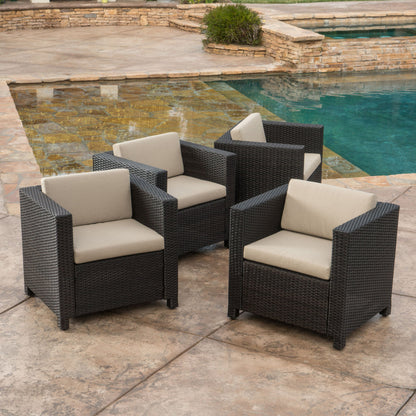 Four Stylish Outdoor Club Chairs With Weather Resistant Cushions in black wicker with light beige cushions are arranged on a stone patio beside a clear pool, with a stone wall and greenery in the background.